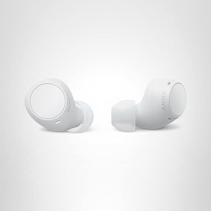 White Sony-style wireless earbuds with charging case on a wooden desk in natural light.